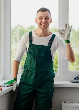 Technician in green overalls standing beside a fitted white window, hand tools laid out on the sill