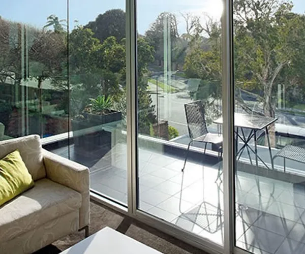 Sitting room behind full-height sliding glazed panels, looking out to a balcony and a tree-lined street