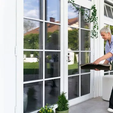 Woman pushing open a tall glazed door from inside a room onto a sunlit garden