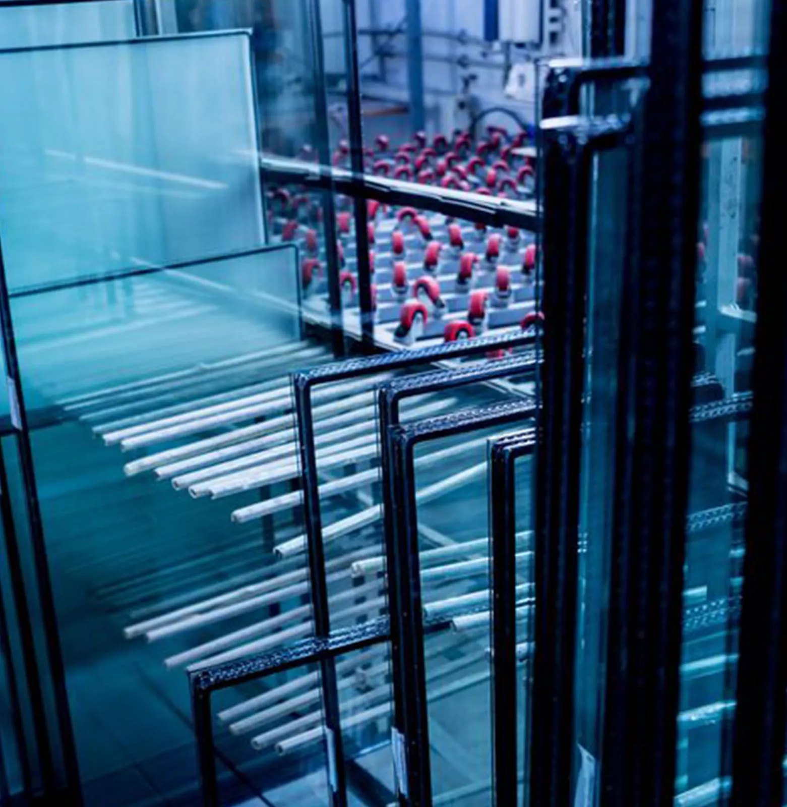 Glass factory floor with stacked panes on racks and insulated-unit spacer frames alongside