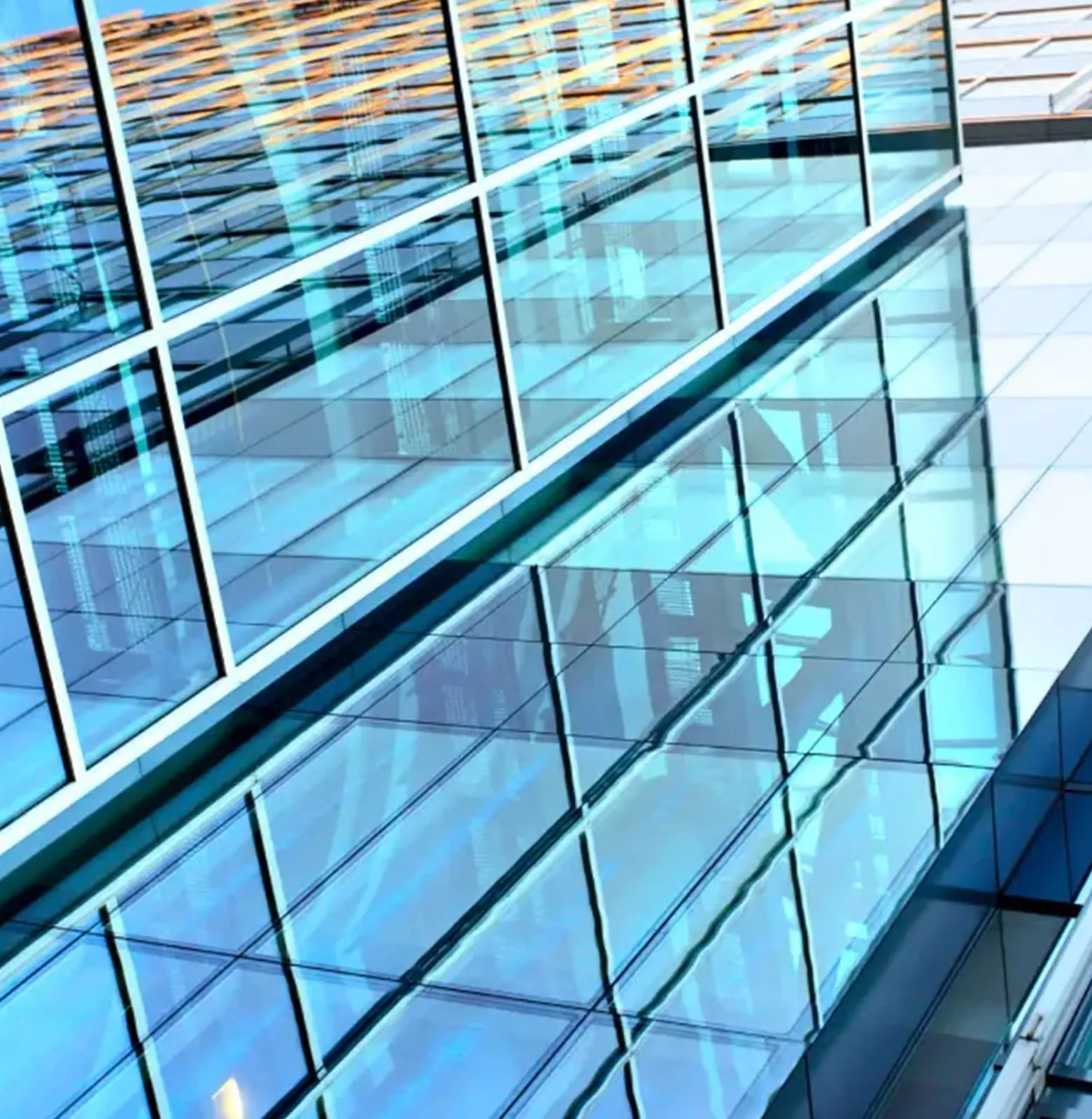 Blue-tinted sloping curtain wall seen from below, sunlight raking across its panels