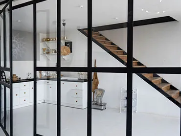 Black steel-framed glazed partition dividing a white kitchen from a staircase landing