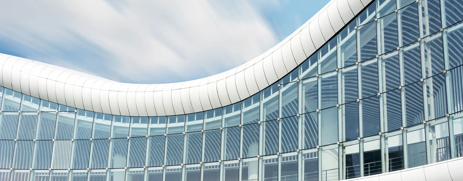 Curved glazed office building rising above street level, its bands of windows catching the light