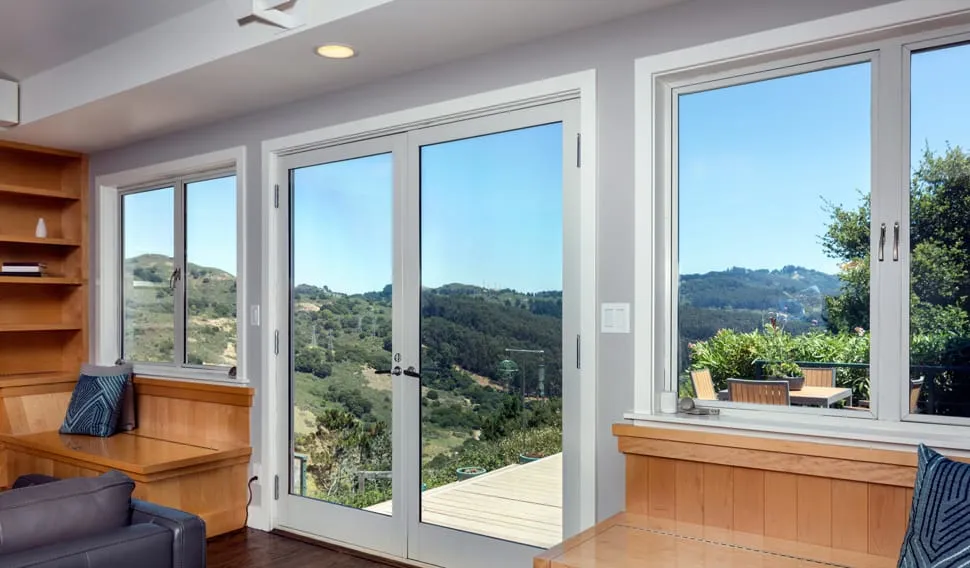 Living room with white French doors and flanking casement windows opening onto a hillside view