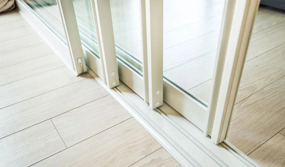 Close-up of the bottom rail and track of a multi-panel sliding door on a pale wood floor