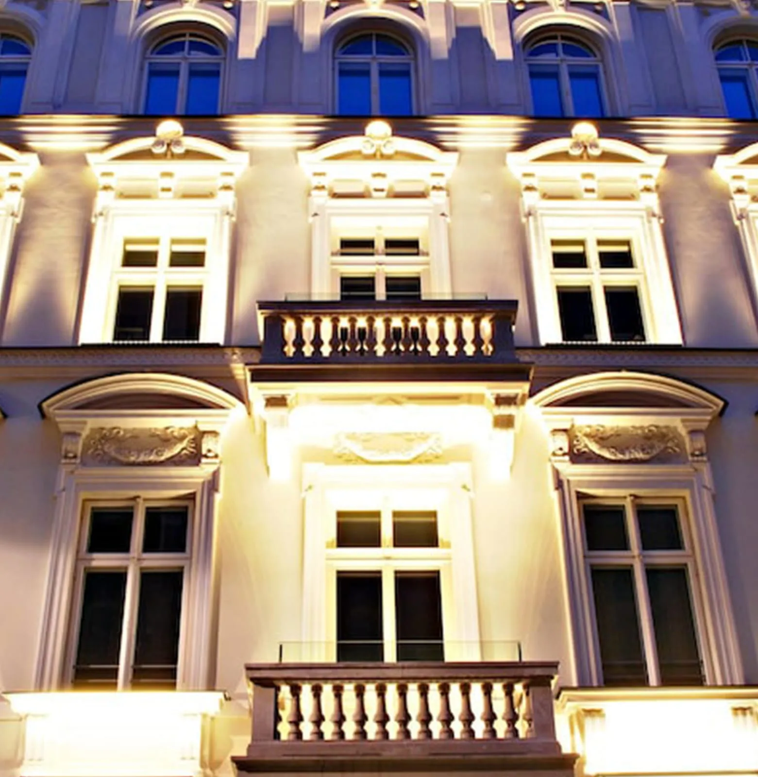 Ornate cream and gold heritage hotel frontage lit up at night, balconied windows on each floor