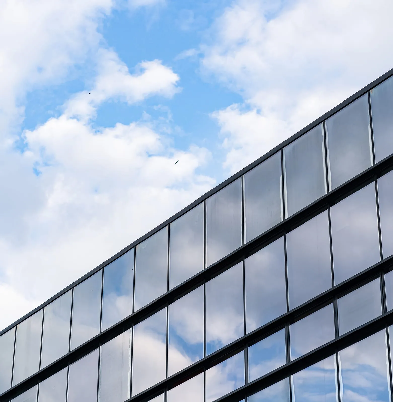 Glazed curtain wall running diagonally against a sky of broken cloud, panels reflecting light