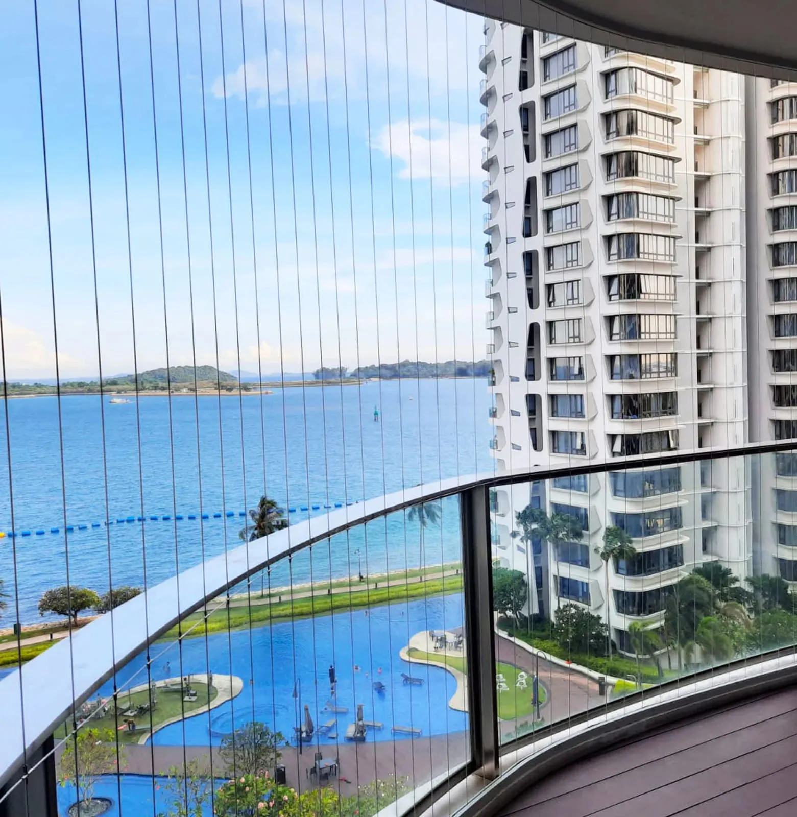 Curved balcony with a fine cable barrier, swimming pool and coastline visible far below
