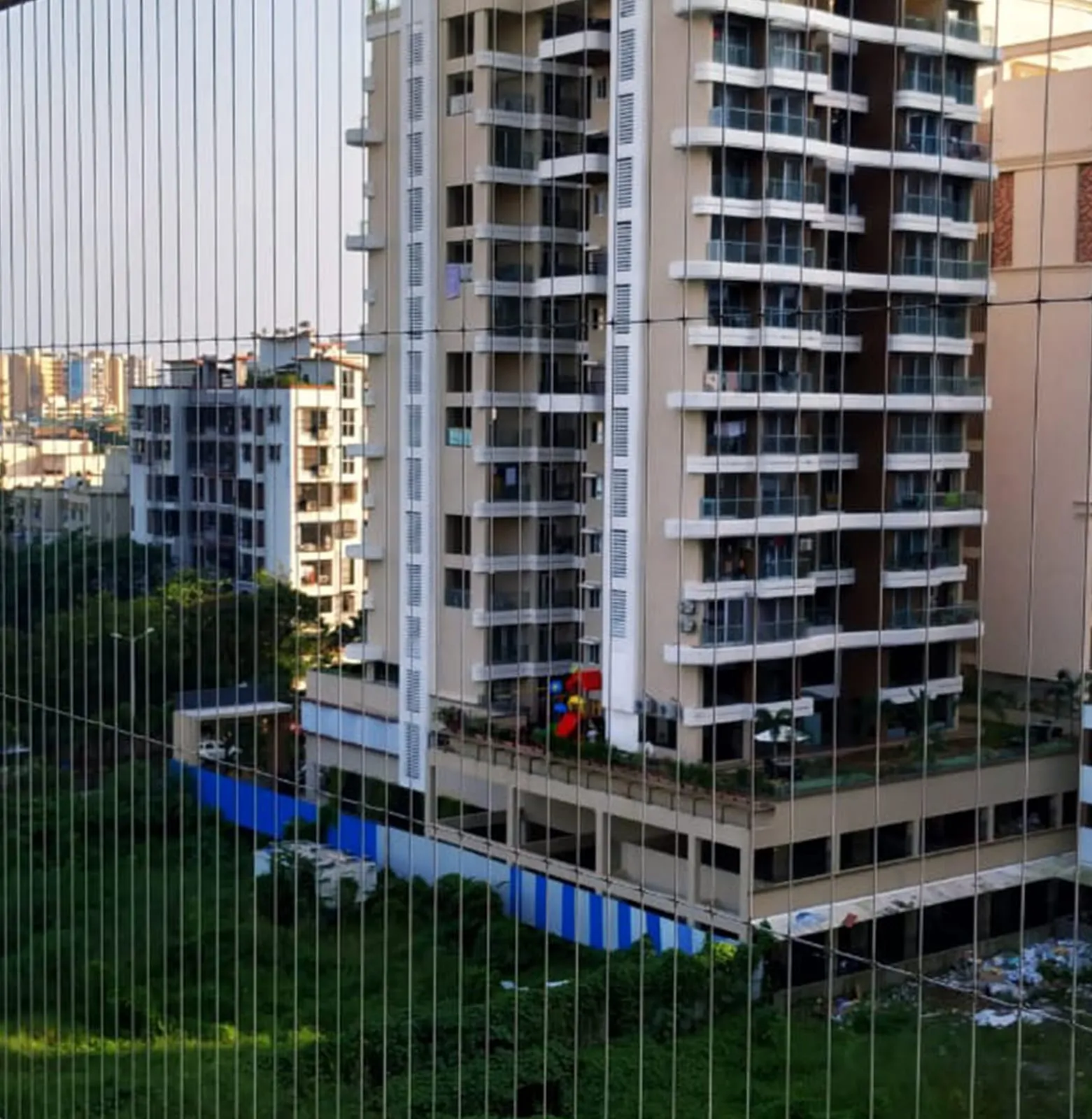 Balcony with fine vertical cables against a view of residential towers and green treetops