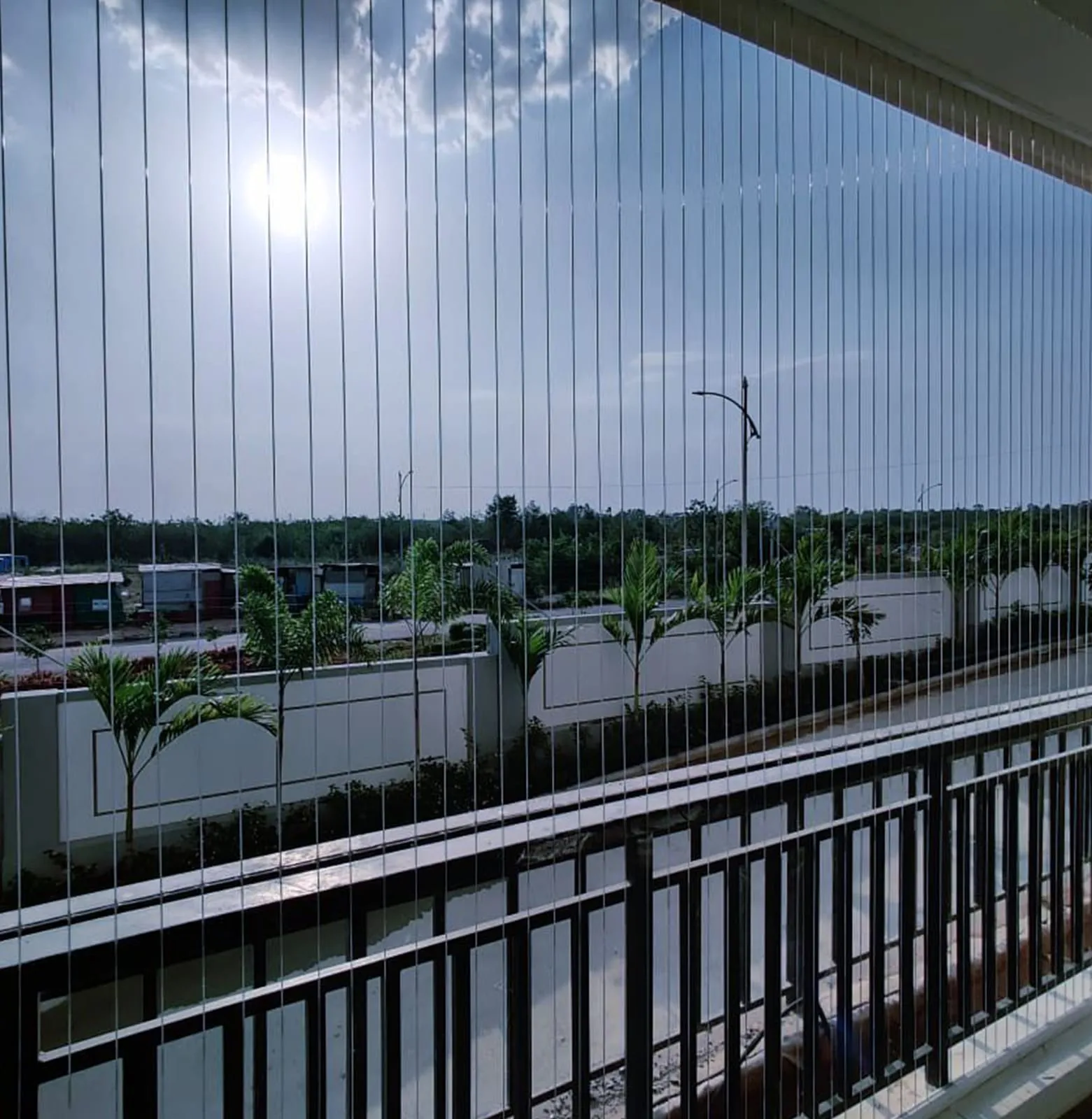 Sunlit balcony strung with horizontal steel cables looking out over low-rise rooftops