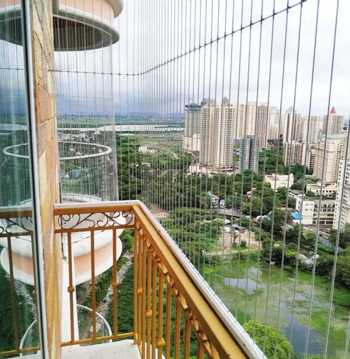 Balcony edged with closely spaced vertical steel cables, high-rise flats and trees beyond