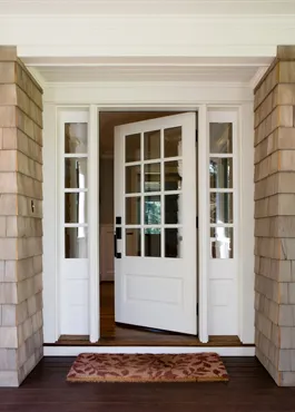 White panelled front door standing open between glazed sidelights in a shingle-clad porch