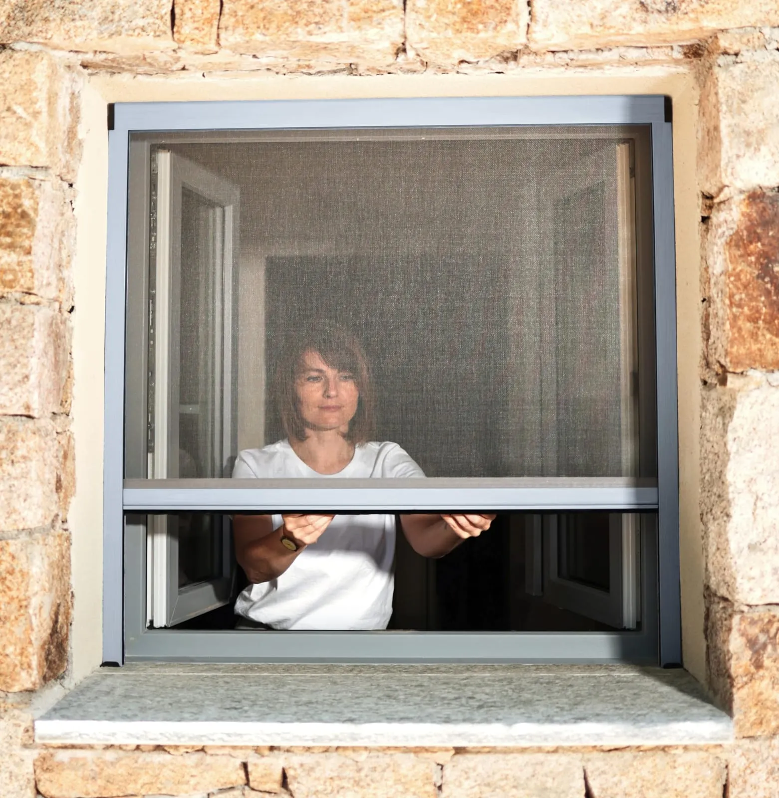 Woman standing at a stone-framed window behind a fitted fine mesh insect screen