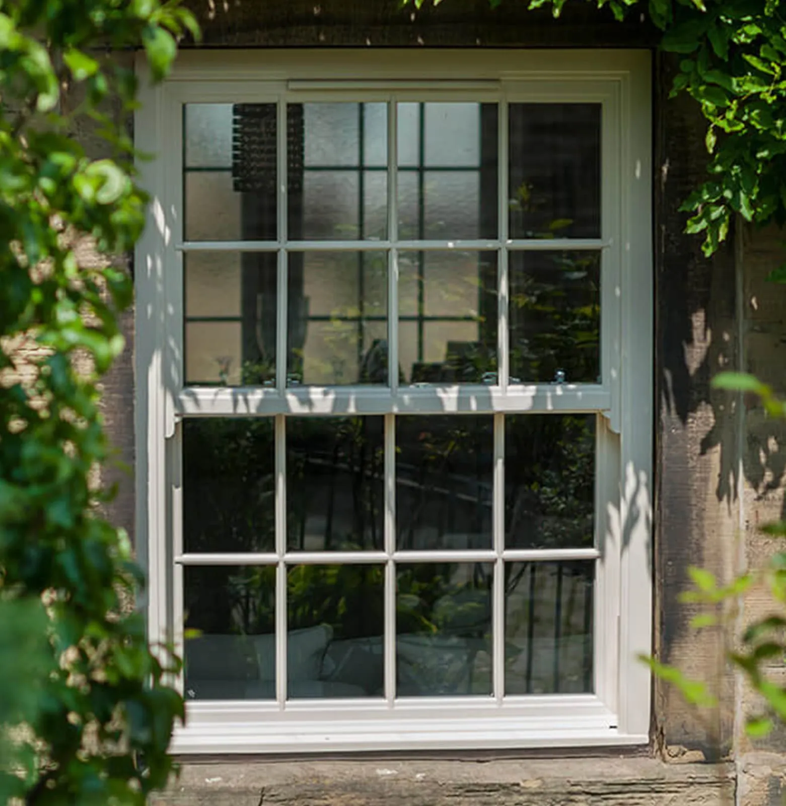 White-painted sash window with glazing bars set in an old wall softened by climbing foliage
