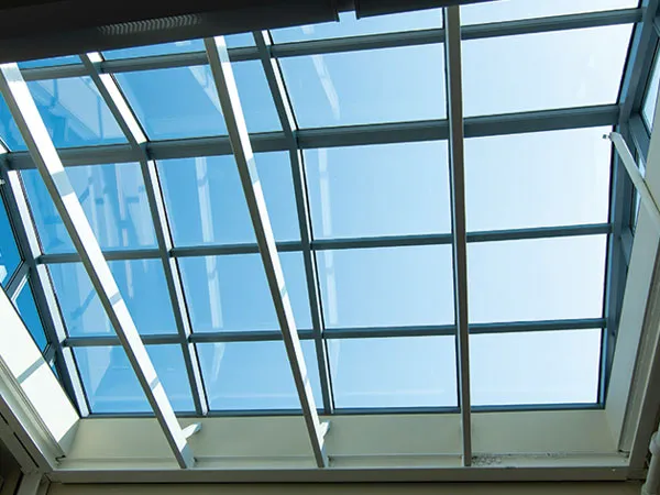 Blue-tinted glazed roof seen from below, its frame grid silhouetted against bright sky