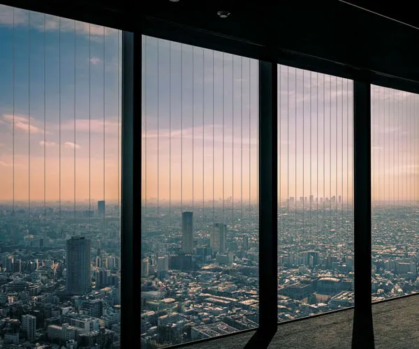 Floor-to-ceiling glazing in a high apartment looking out over a city skyline at sunset