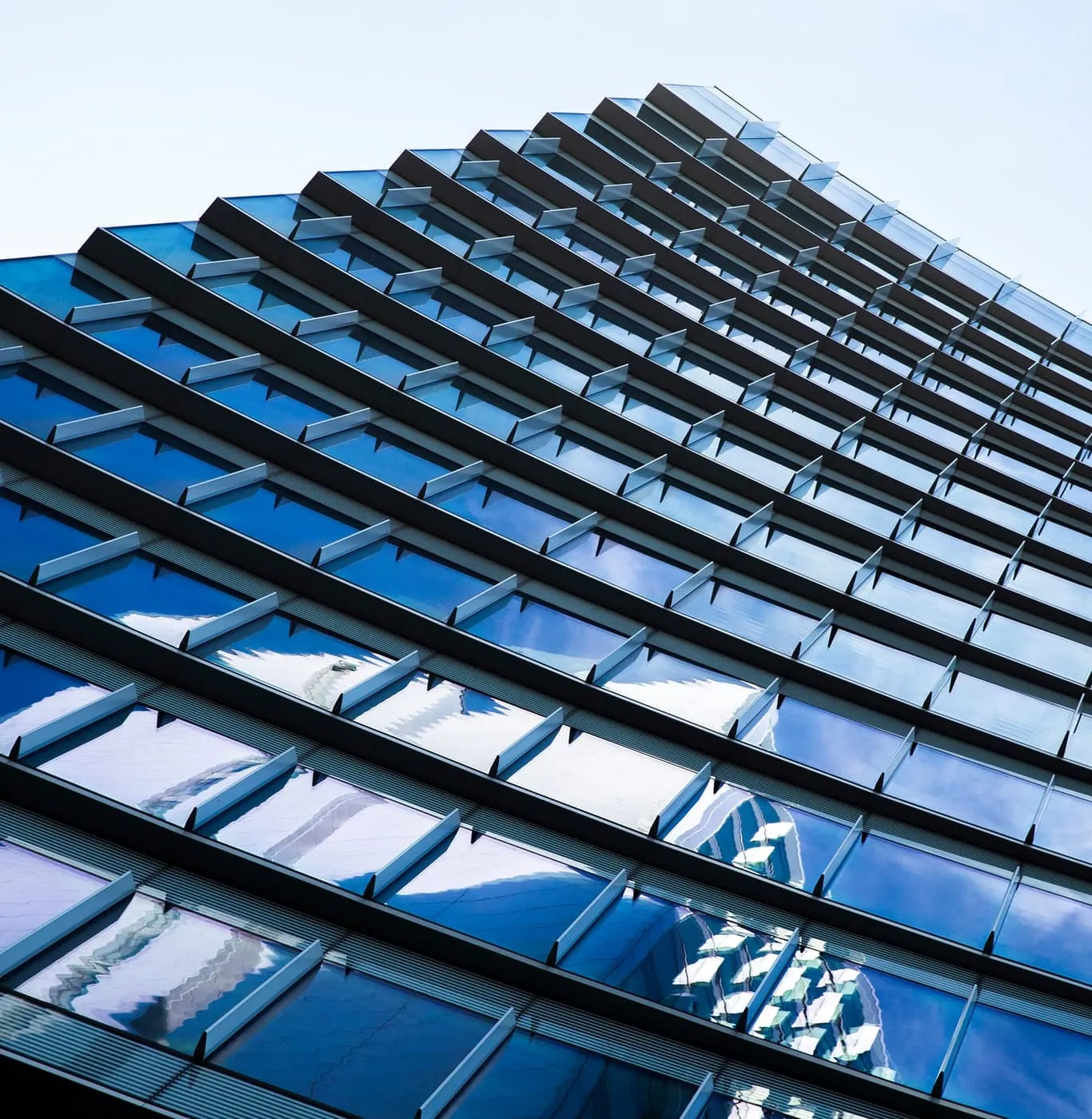 Sloping blue glazed façade seen from below, its grid of mullions and transoms silhouetted