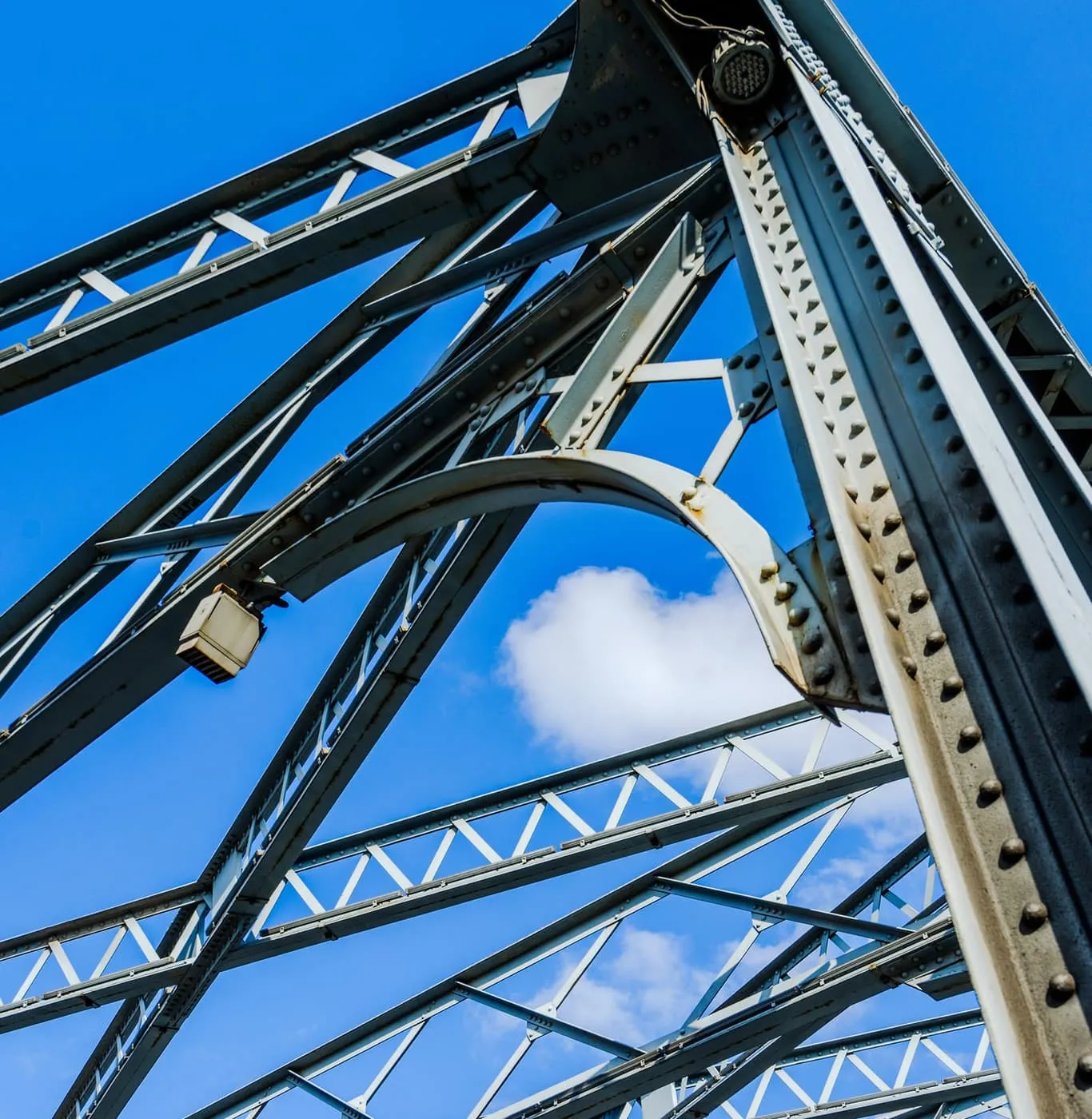 Dark steel arch truss curving overhead against a sky of scattered white cloud